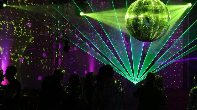 Wide shot of partygoers dancing beneath a disco ball in a laser-lit dance venue Wide shot of partygoers dancing beneath a disco ball in a laser-lit dance venue