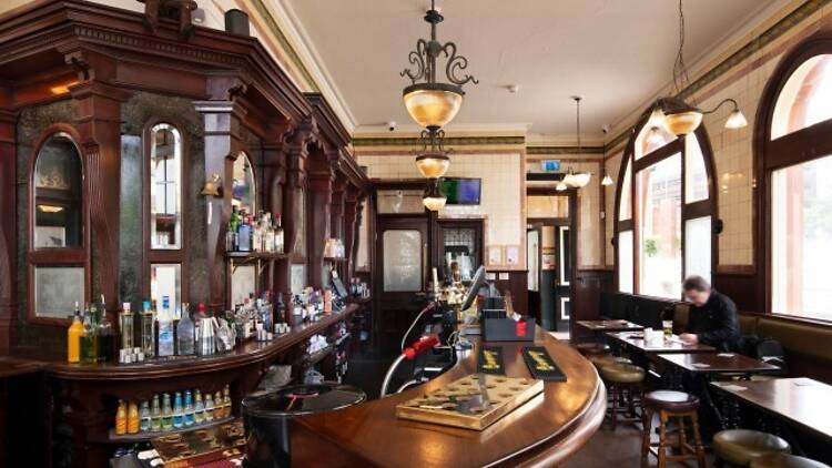 The interior of the Woodman, it features wooden bar, historic lighting, and small tables by arched windows.