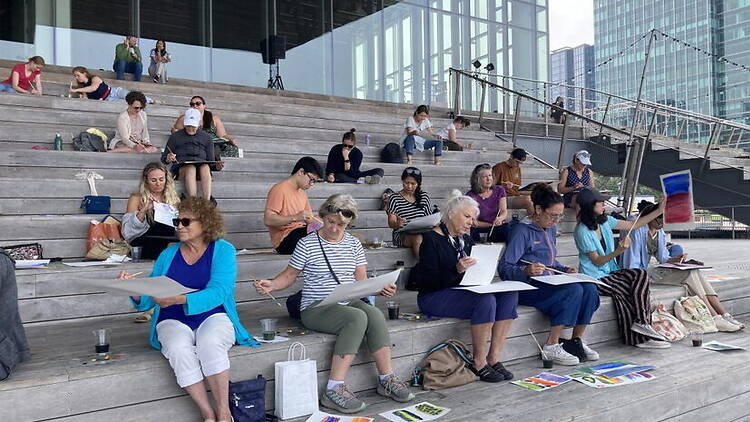 A wide shot of people painting while sitting on stairs. A wide shot of people painting while sitting on stairs.