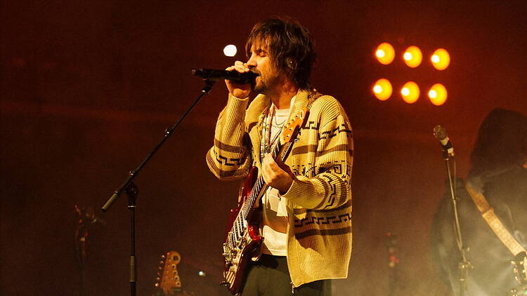 A close-up shot of Tame Impala singing on stage with a guitar.