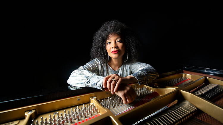 A wide shot of Zahili Zamora leaning on an open grand piano. A wide shot of Zahili Zamora leaning on an open grand piano.