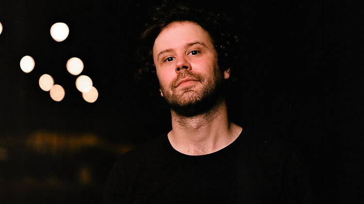 Medium close-up of a person looking at the camera against a dark background with blurred lights Medium close-up of a person looking at the camera against a dark background with blurred lights
