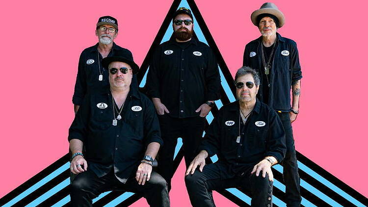 Wide shot of a five-member band posing against a pink graphic background Wide shot of a five-member band posing against a pink graphic background