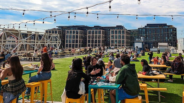 Wide shot of people socializing and eating at tables on a rooftop terrace in an urban outdoor space