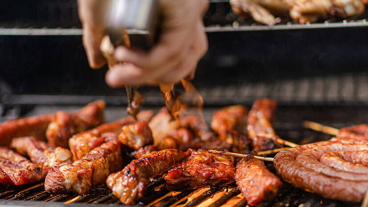 Close-up shot of a hand using tongs to flip sizzling meat on a hot backyard grill Close-up shot of a hand using tongs to flip sizzling meat on a hot backyard grill