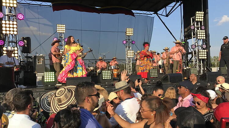 Wide shot of a large crowd watching a traditional music band perform on an outdoor stage Wide shot of a large crowd watching a traditional music band perform on an outdoor stage