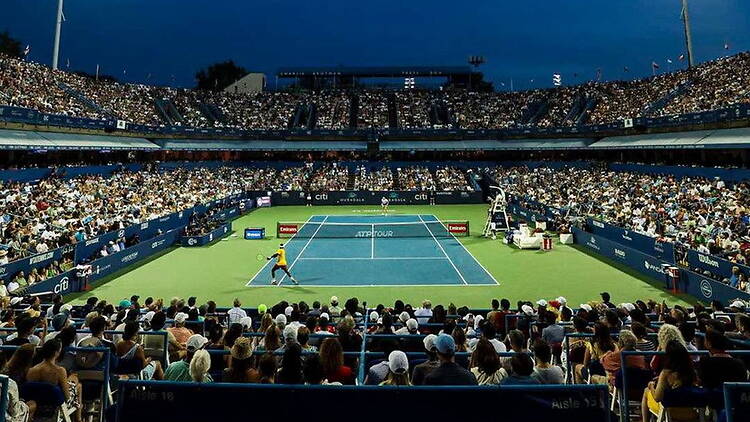 A wide shot of players competing in a tennis match at an arena. A wide shot of players competing in a tennis match at an arena.