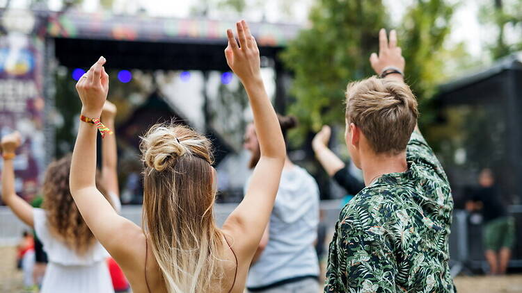 A wide shot of people raising their hands toward an outdoor stage. A wide shot of people raising their hands toward an outdoor stage.