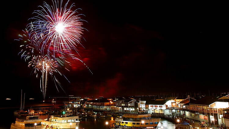Wide shot of fireworks exploding above a waterfront marina at night Wide shot of fireworks exploding above a waterfront marina at night