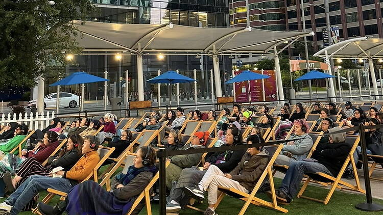 Wide shot of people relaxing in lounge chairs at an outdoor movie screening in an urban plaza Wide shot of people relaxing in lounge chairs at an outdoor movie screening in an urban plaza