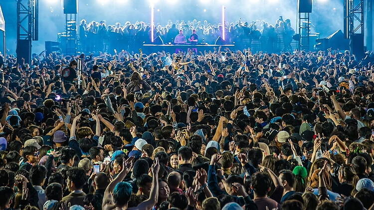 Wide shot of a large crowd dancing in front of DJs performing on a concert stage.