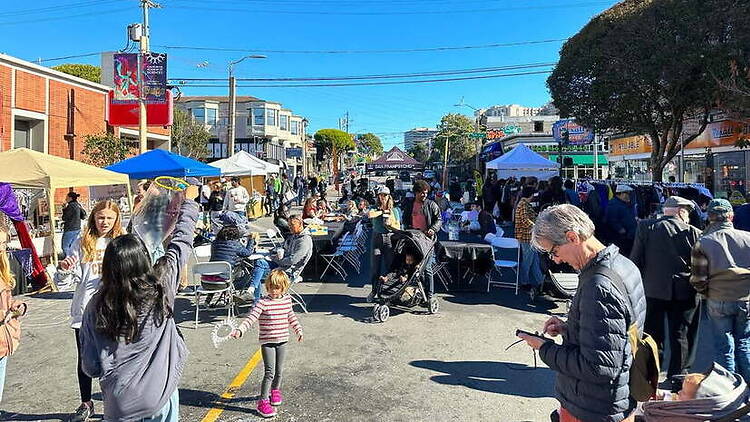 Wide shot of people browsing vendor booths and activities at an outdoor street market. Wide shot of people browsing vendor booths and activities at an outdoor street market.