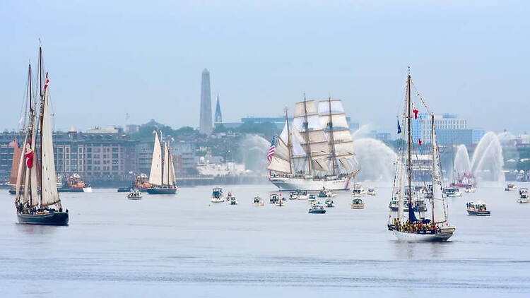 A wide shot of tall ships sailing across a harbor with smaller boats nearby. A wide shot of tall ships sailing across a harbor with smaller boats nearby.