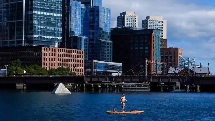 A wide shot of a person standing on a paddleboard in a river. A wide shot of a person standing on a paddleboard in a river.