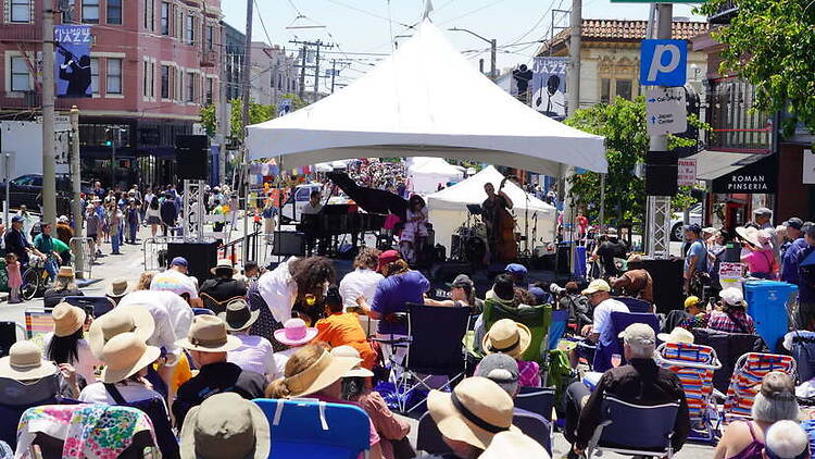 Wide shot of a crowd sitting in lawn chairs and watching a band perform under a large white tent Wide shot of a crowd sitting in lawn chairs and watching a band perform under a large white tent