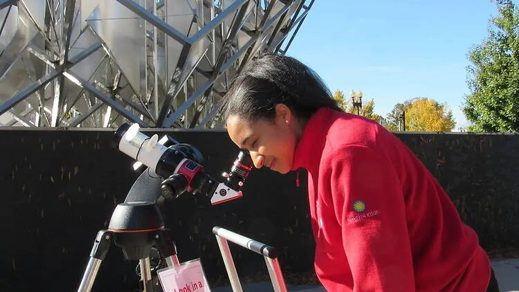 A wide shot of a woman peeking through a telescope A wide shot of a woman peeking through a telescope