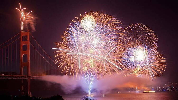 Wide shot of vibrant fireworks exploding over the water next to a bridge Wide shot of vibrant fireworks exploding over the water next to a bridge