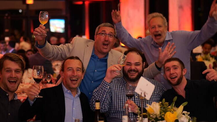 A close-up of people raising glasses at an indoor event. A close-up of people raising glasses at an indoor event.