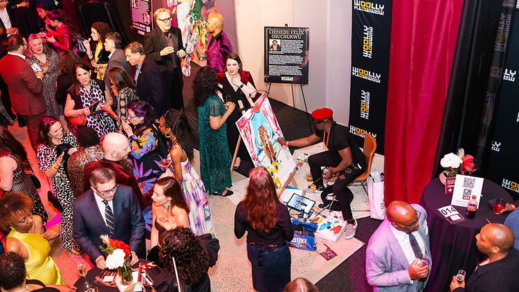 A wide shot of people socializing while an artist paints at an indoor event A wide shot of people socializing while an artist paints at an indoor event