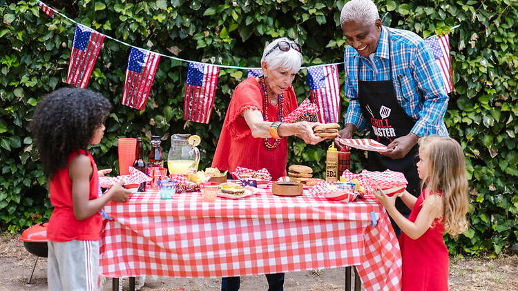 Wide shot of a family having a picnic at an outdoor table decorated with American flags. Wide shot of a family having a picnic at an outdoor table decorated with American flags.