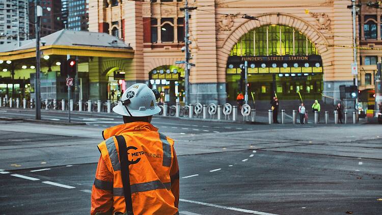 Metro Tunnel worker man in orange and black backpack walking on pedestrian lane during daytime