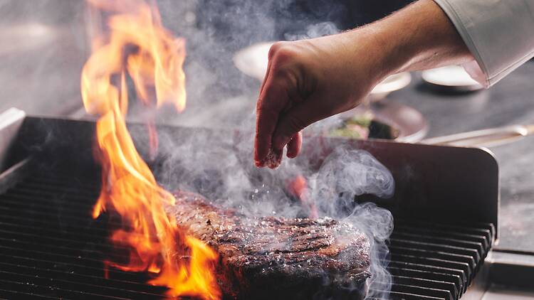 Altitude Shangri-La Sydney a chef salting a piece of meat on a grill