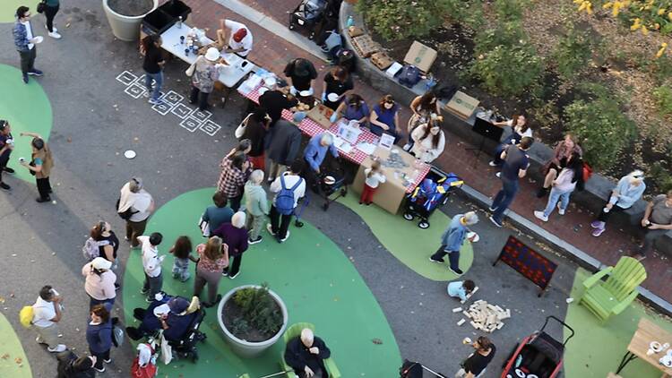 wide shot of people gathering at activity tables in an outdoor plaza wide shot of people gathering at activity tables in an outdoor plaza