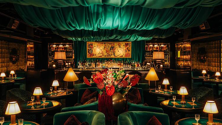 A lounge with green drapery on the ceiling, plush seating and dim lighting.