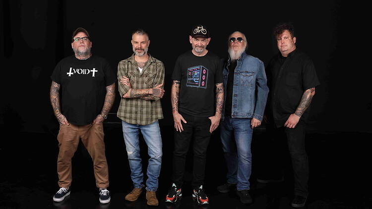 Wide shot of a five-member band posing against a black studio background. Wide shot of a five-member band posing against a black studio background.