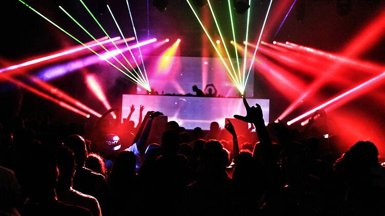 Wide shot of a crowd dancing in front of a DJ booth under colorful laser lights Wide shot of a crowd dancing in front of a DJ booth under colorful laser lights