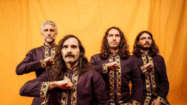 Medium shot of a four-member band posing against a yellow backdrop. Medium shot of a four-member band posing against a yellow backdrop.