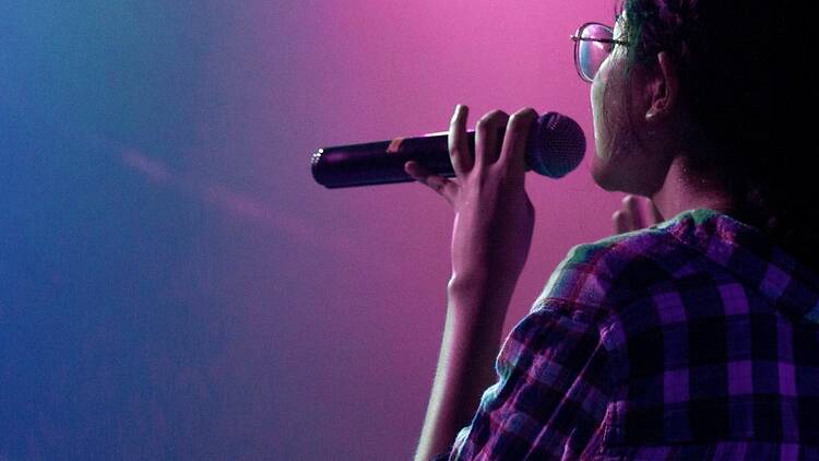 Profile view of a person singing into a microphone on a stage illuminated by colorful lights. Profile view of a person singing into a microphone on a stage illuminated by colorful lights.