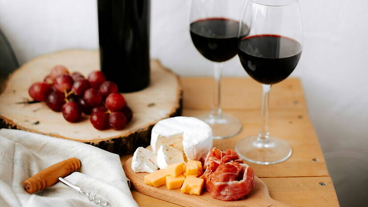 Wide shot view of a wine and cheese spread with red grapes and two glasses of red wine on a wooden surface. Wide shot view of a wine and cheese spread with red grapes and two glasses of red wine on a wooden surface.