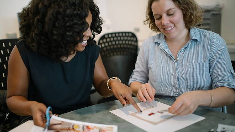 Medium shot of two people collaborating on a paper craft project at a table. Medium shot of two people collaborating on a paper craft project at a table.