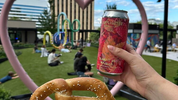 Close-up view of a hand holding a drink and a pretzel in an outdoor lawn. Close-up view of a hand holding a drink and a pretzel in an outdoor lawn.