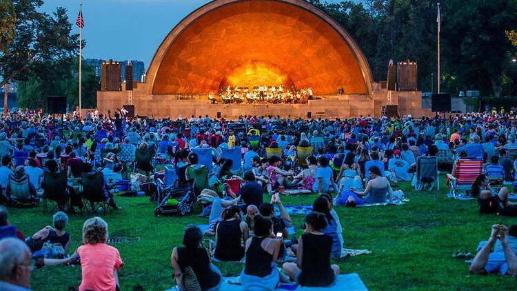 Wide view of a crowd watching a concert at an outdoor amphitheater. Wide view of a crowd watching a concert at an outdoor amphitheater.