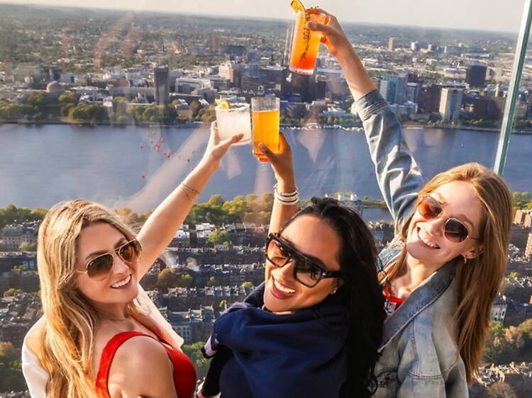 High-angle view of three women raising drinks above a city skyline. High-angle view of three women raising drinks above a city skyline.