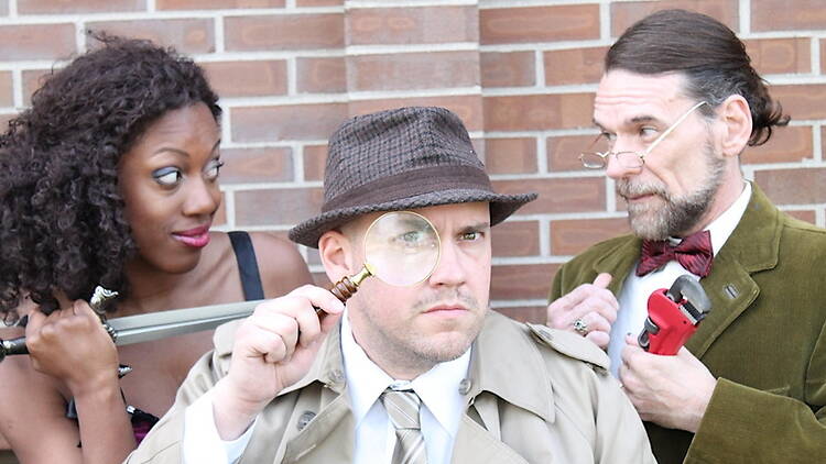 Front view of three people posing in detective-themed costumes against a brick wall. Front view of three people posing in detective-themed costumes against a brick wall.