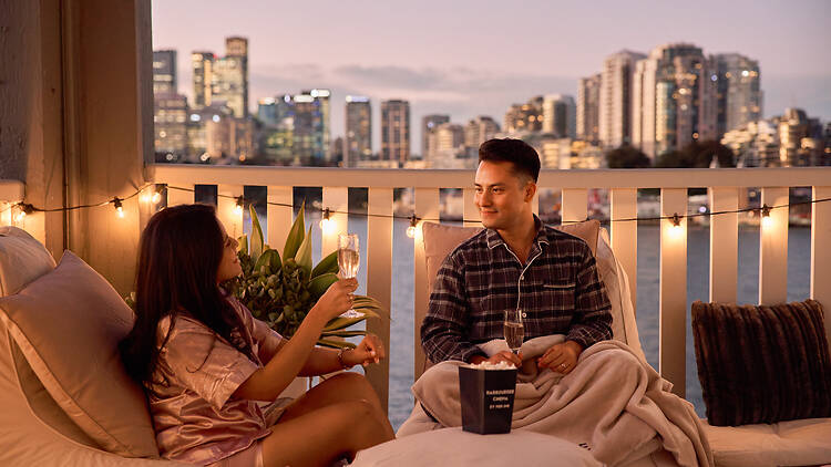 Harbourside Cinema by Pier One man and women in pyjamas enjoy wine and popcorn with Sydney harbour background