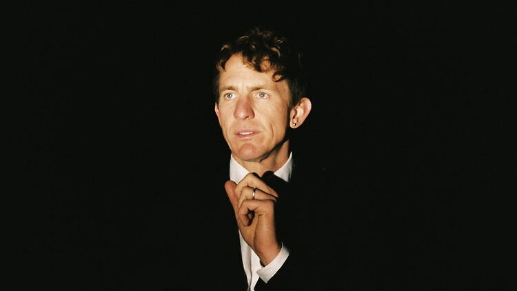 Medium close-up view of a person in a black suit staring out in a dark stage. Medium close-up view of a person in a black suit staring out in a dark stage.