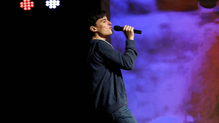 A close-up of a person singing into a microphone on a stage A close-up of a comedian performing on a stage with a microphone