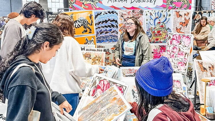 A wide shot of people browsing artwork at an artist's booth A wide shot of people browsing artwork at an artist's booth