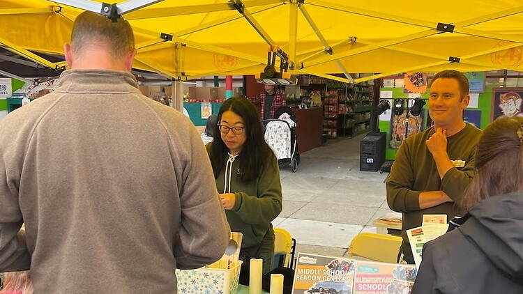 A wide shot of people browsing a market stall under a canopy. A wide shot of people browsing a market stall under a canopy.