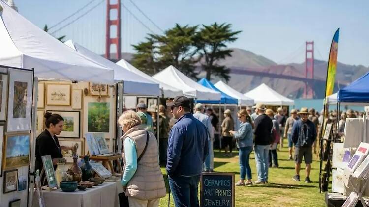 A wide shot of people browsing an outdoor arts and crafts market A wide shot of people browsing an outdoor arts and crafts market
