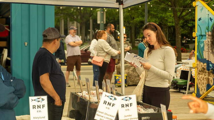 A wide shot of people browsing seafood products at an outdoor market. A wide shot of people browsing seafood products at an outdoor market.