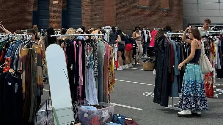 A wide shot of people browsing clothing racks at an outdoor market. A wide shot of people browsing clothing racks at an outdoor market.