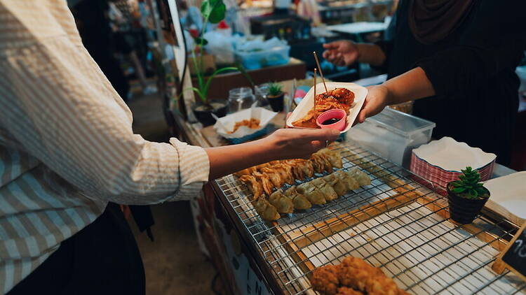 A close-up of a person receiving food from a vendor at a market stall. A close-up of a person receiving food from a vendor at a market stall.
