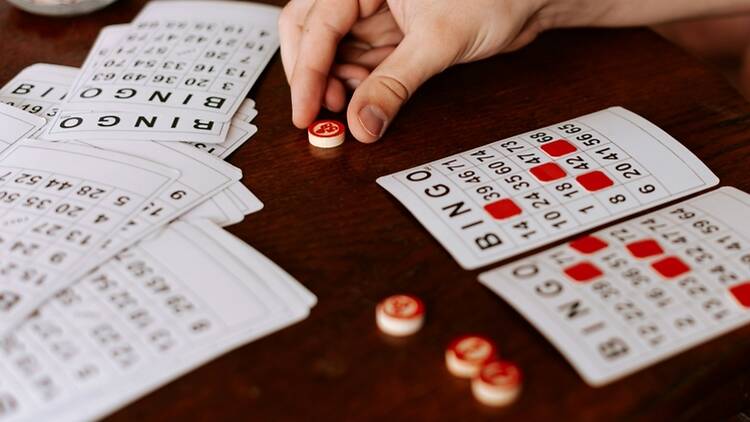 A close-up of a hand placing a bingo marker on bingo cards on a table. A close-up of a hand placing a bingo marker on bingo cards on a table.
