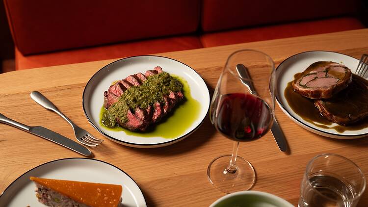 Bavette steak with chimichurri on a table with wine and other plates 