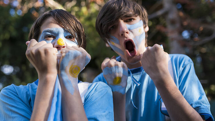 Friends cheering for the Argentine soccer team during the match. Fans of the Argentine soccer team, painted with the colors of Argentina cheering in the World Cup.